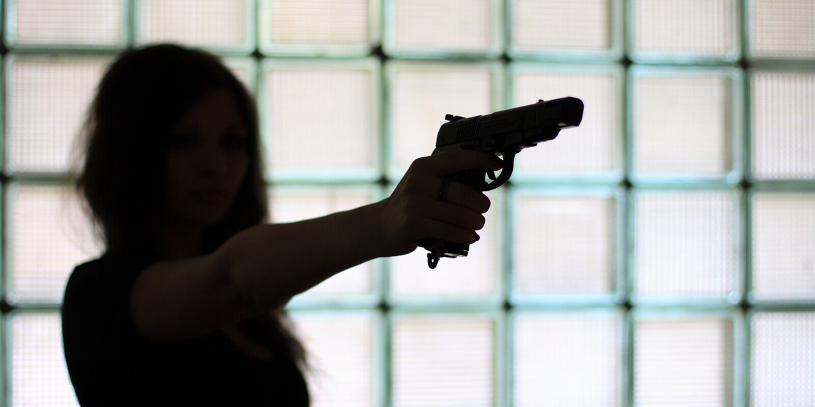 silhouette of a woman with a gun on a glass wall background